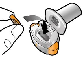 A hand opens the white and orange medical device by removing the protective cap to expose the
