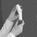 Dos manos con bata blanca sostienen y manipulan un dispositivo médico cilíndrico blanco y oscuro sobre un fondo gris uniforme