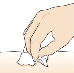 A hand holding a white tissue to clean or dab a smooth, light skin area