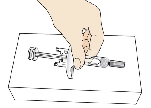 A hand holding a pre-filled syringe horizontally placed on a flat white surface for drug preparation