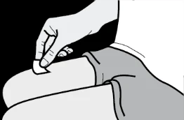 Una mano aplica una pequeña tirita blanca sobre la piel del muslo de una persona sentada que lleva puestos pantalones cortos