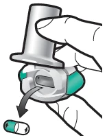 A hand pressing a cylindrical medical device onto a container to release a green and white capsule, indicated by a black arrow