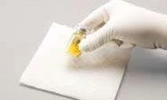 A hand wearing a white glove holding a small glass vial containing yellow liquid above a white sterile gauze on a gray background
