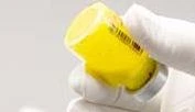 A hand wearing a white glove holding and tilting a yellow plastic bottle with a