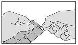 Two hands tearing a sheet with small square tablets along dotted lines to separate the medication