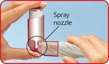 Mani che tengono un inalatore bianco e rosso con una linea evidenziata che indica la bocchetta dello spray e un cerchio sulla parte inferiore del dispositivo