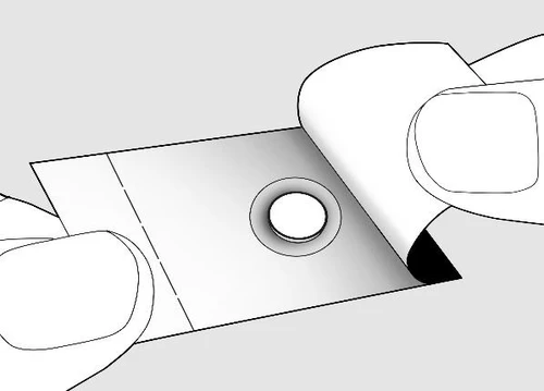 Hands tearing open a white medication package, revealing a round opening with a visible tablet placed in the center