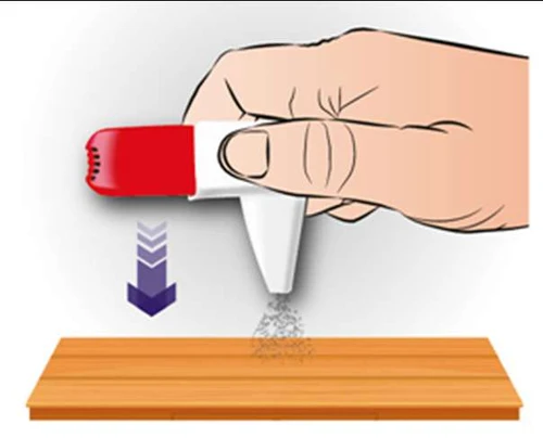 Una mano impugna un dispositivo medico rosso e bianco dal quale fuoriesce una polvere fine su una superficie di legno, sotto una freccia viola diretta verso il basso