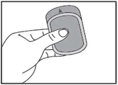 Mano che tiene con un dito un dispositivo medico di forma arrotondata per l'applicazione di un farmaco, con una freccia visibile che indica la direzione dell'azione