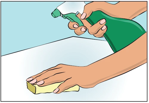 Hands holding a green spray bottle and another hand wiping a light-colored table surface with a white sponge
