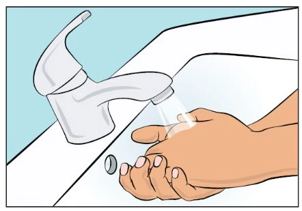 Hands under soap under a stream of water flowing from a white faucet mounted above a white sink on a light blue background