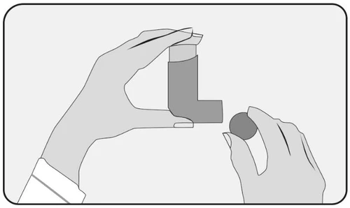 Two hands holding an L-shaped inhaler and a circular component, preparing the device for use in the medication delivery process