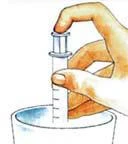 Hand holding a transparent syringe with scale markings vertically above a white container or dish on a light background