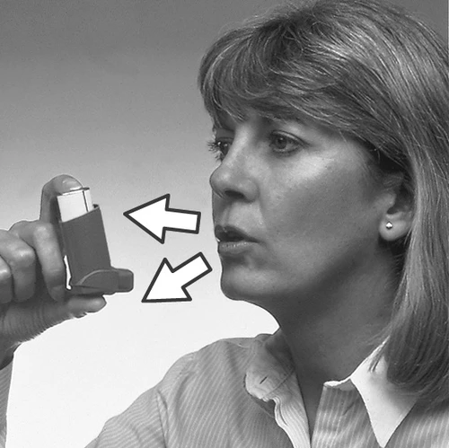 Una donna tiene l'inalatore vicino alla bocca, con due frecce bianche che indicano la direzione dell'avvicinamento del dispositivo al viso per assumere il farmaco