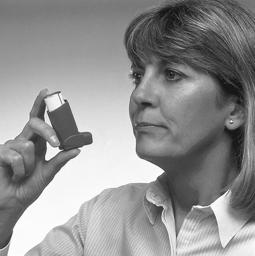 Una donna con una camicia chiara tiene l'inalatore in mano, osservando attentamente il dispositivo su uno sfondo uniforme chiaro