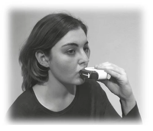 A young woman holding a white inhaler to her mouth, preparing to take a dose of medication to ease breathing