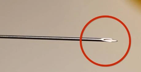 Primer plano de la punta afilada de una aguja médica metálica, cuyo extremo está resaltado con un círculo rojo sobre fondo claro