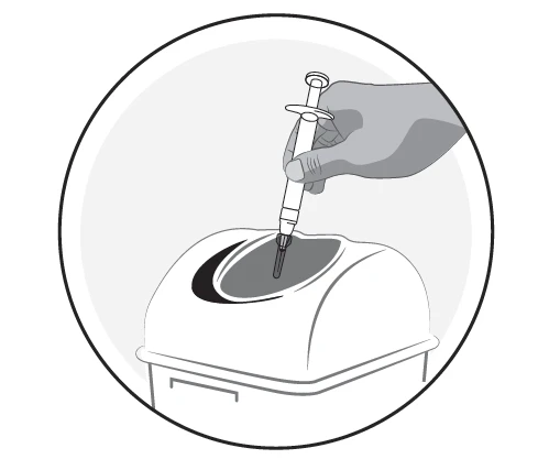 Mano che tiene una siringa con ago inserita in un foro su un contenitore bianco per rifiuti sanitari posizionato su una superficie piana