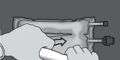 Hands squeezing a flexible fluid bag, directing the medication stream toward two plastic connectors with valves on the right side