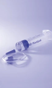 Прозора шприц-секція із написом BD Plastipak, розташована поруч із від'єднаною голкою на світлому блакитному тлі