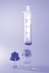 Siringa trasparente con scala graduata in millilitri posizionata verticalmente sopra una fiala di vetro con liquido e un tappo scuro separato su sfondo chiaro
