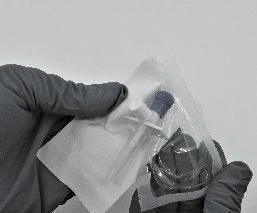 Руки в сірих рукавичках тримають стерильну упаковку, що містить ампулу з темним корком, і білий медичний елемент на світлому тлі