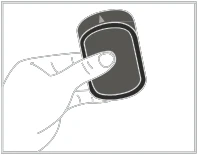 Mano sosteniendo un medicamento u dispositivo médico oscuro, rectangular, con una flecha blanca visible en la parte superior, apuntando hacia la derecha
